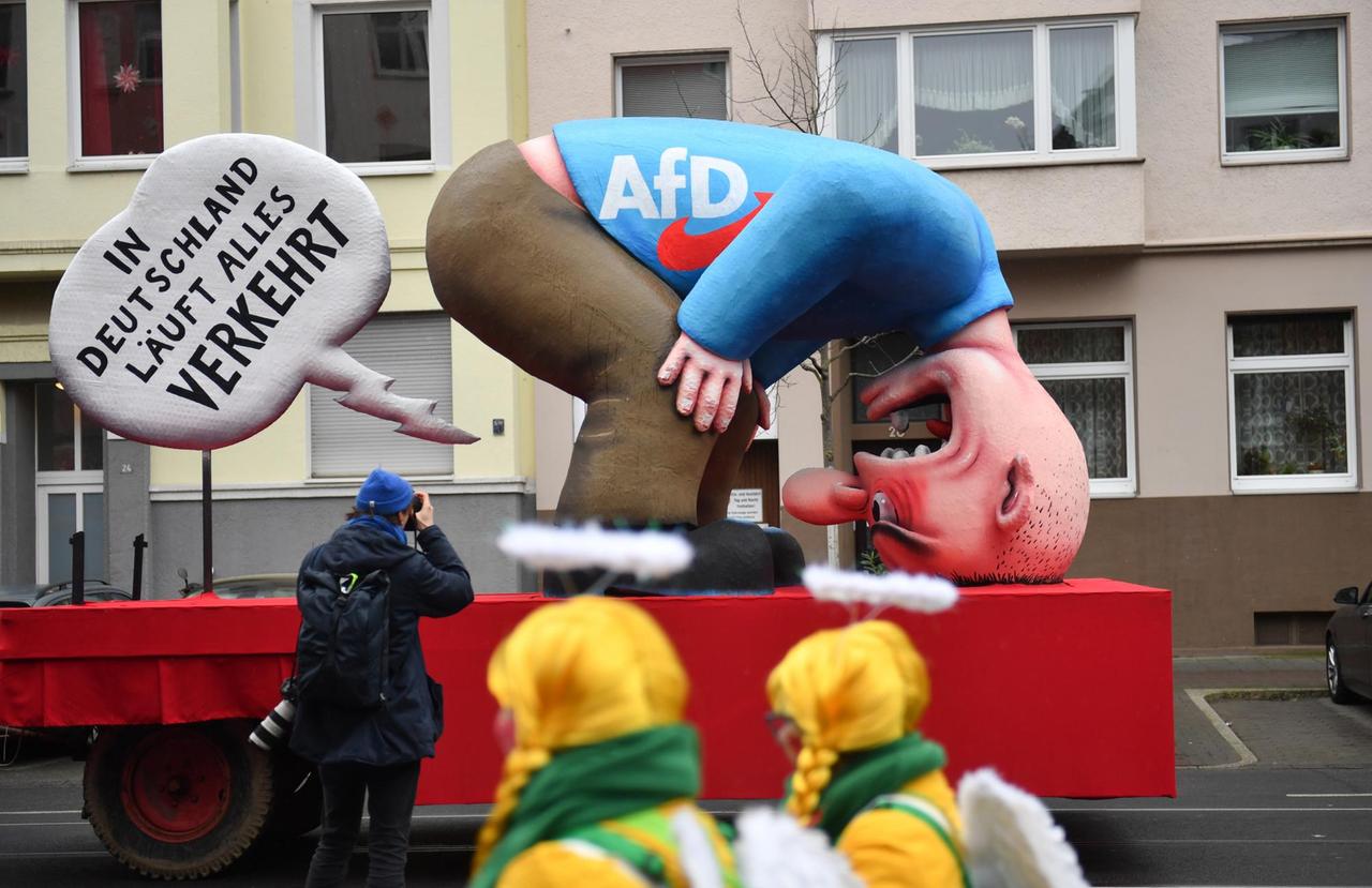Jecken beobachten einen Fotografen am Motivwagen AfD vor dem Rosenmontagszug. Jecken beobachten einen Fotografen am Motivwagen AfD vor dem Rosenmontagszug.