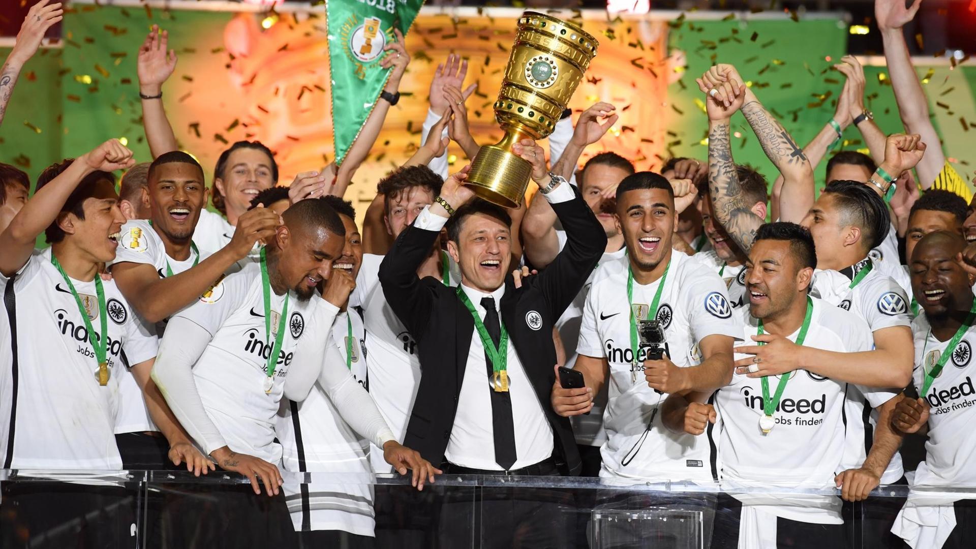 Trainer Niko Kovac (M) von Eintracht Frankfurt und seine Spieler jubeln über dem Sieg mit dem Pokal bei der Siegerehrung auf dem Podium.