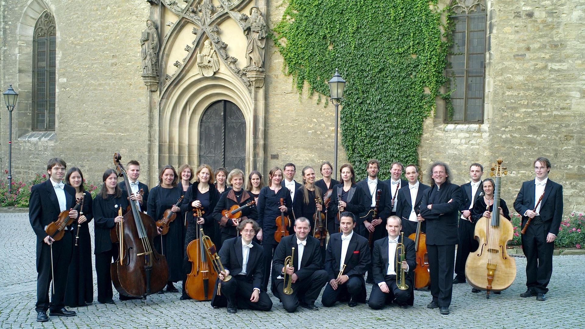 Das Orchester steht vor einem prächtigen Kirchenportal.