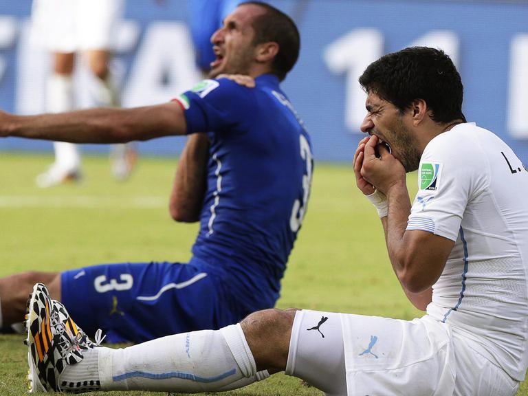 Der italienische Abwehrspieler Giorgio Chiellini (l) weist auf seine Schulter, in die Uruguays Stürmer Luis Suárez (r) gebissen hat. Chiellini hält sich die Schulter, Suarez fasst an seine Zähne.