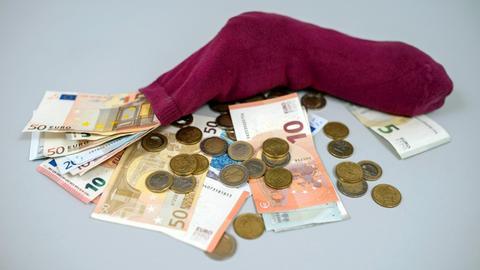Geldscheine und Münzen stecken in einem Strumpf.