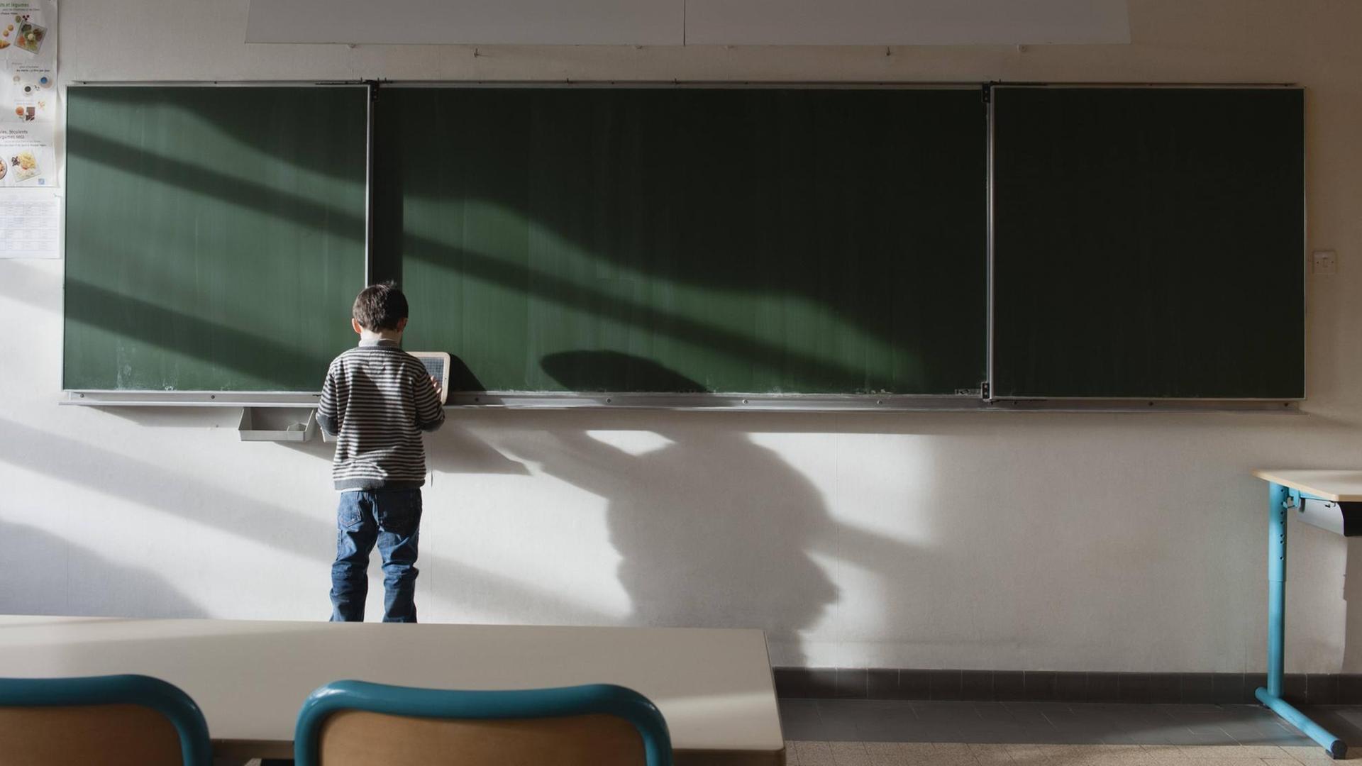 Ein Junge steht an einer Tafel im leeren Klassenraum.