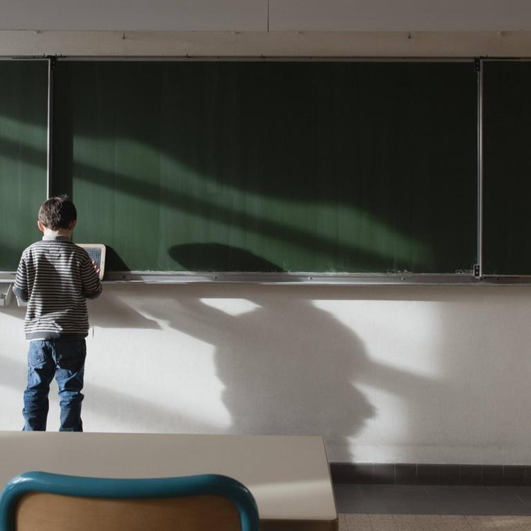 Ein Junge steht an einer Tafel im leeren Klassenraum.