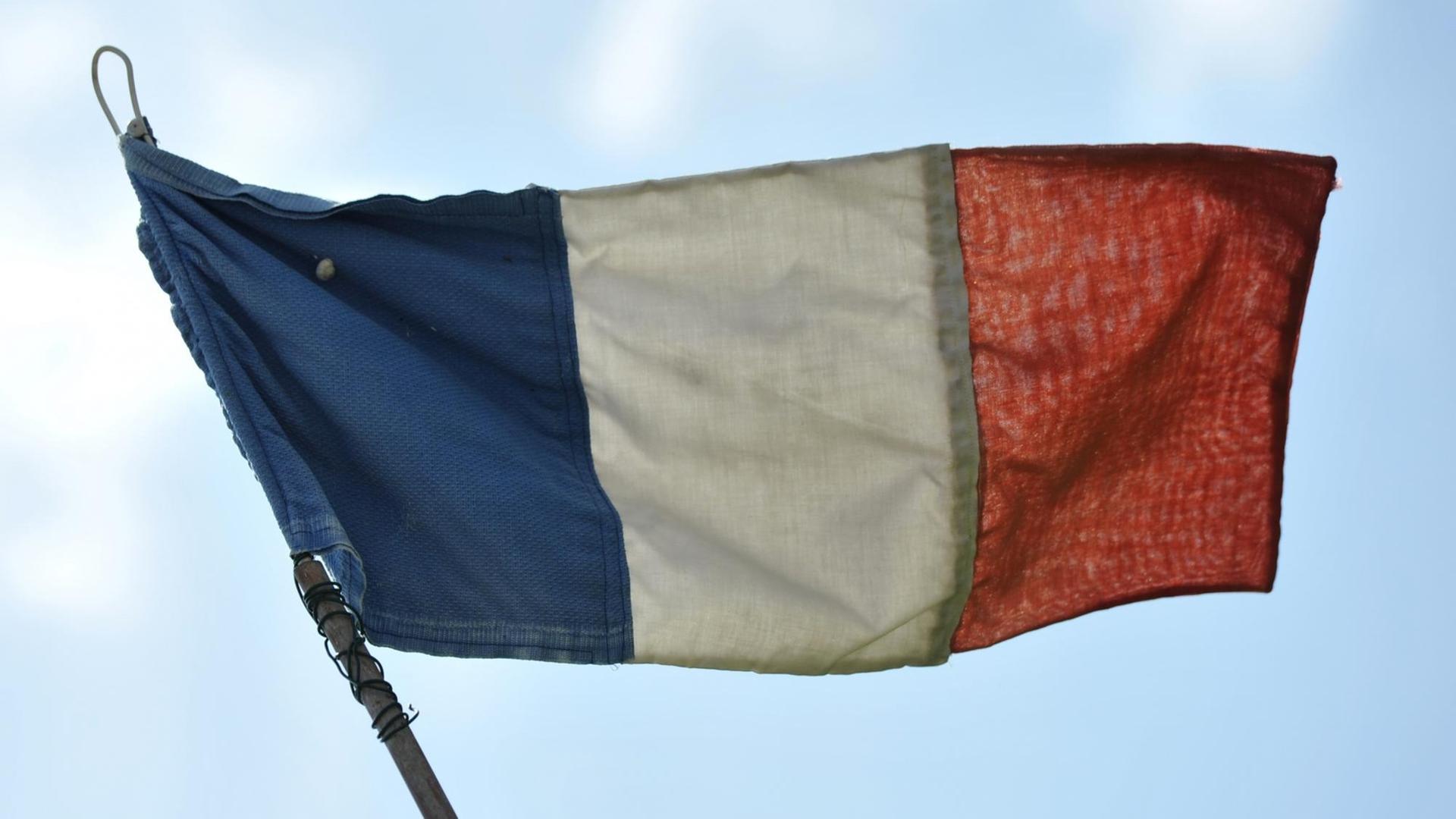 Eine französische Flagge flattert im Wind, dahinter sieht man blauen Himmel mit hellen Wolken