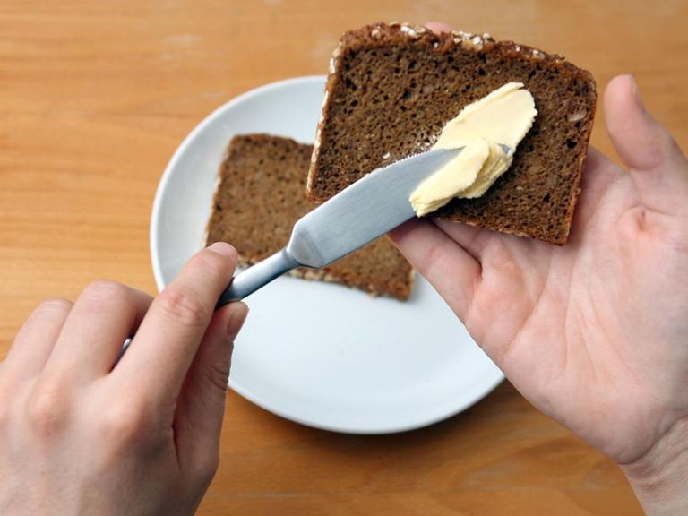 Ein Linkshänder schmiert Butter auf eine Scheibe Brot.