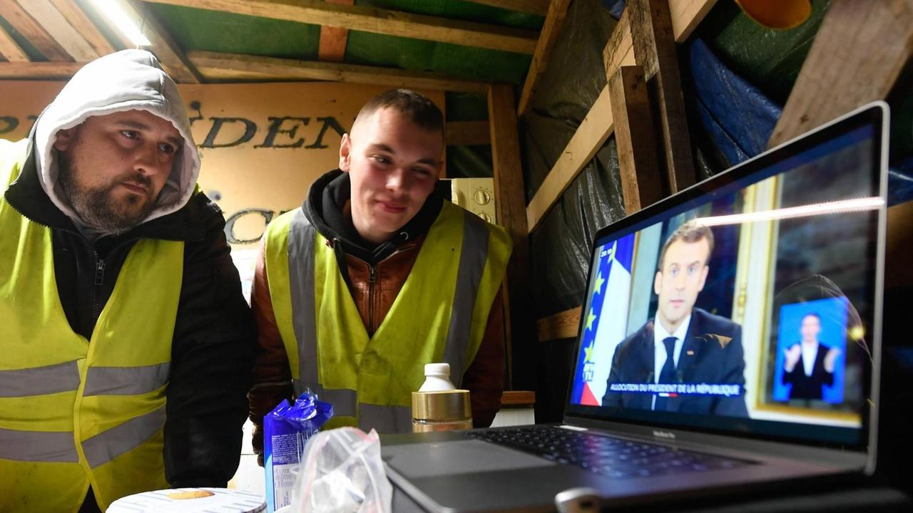 Die zwei Protestler - sogenannte Gelbwestler - verfolgen die Übertragung der Ansprache des französischen Präsidenten Emmanuel Macron