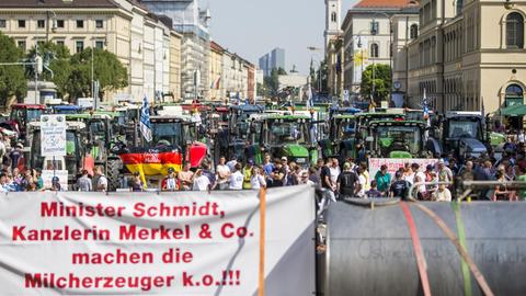 Zahlreiche Traktoren stehen am 01.09.2015 in der Ludwigstraße in München (Bayern), während im Vordergrund ein Transparent mit der Aufschrift "Minister Schmidt, Kanzlerin Merkel & Co. machen die Milcherzeuger k.o.!!!". Hunderte Landwirte protestieren gegen sinkende Milchpreise. Foto: Marc Müller/dpa