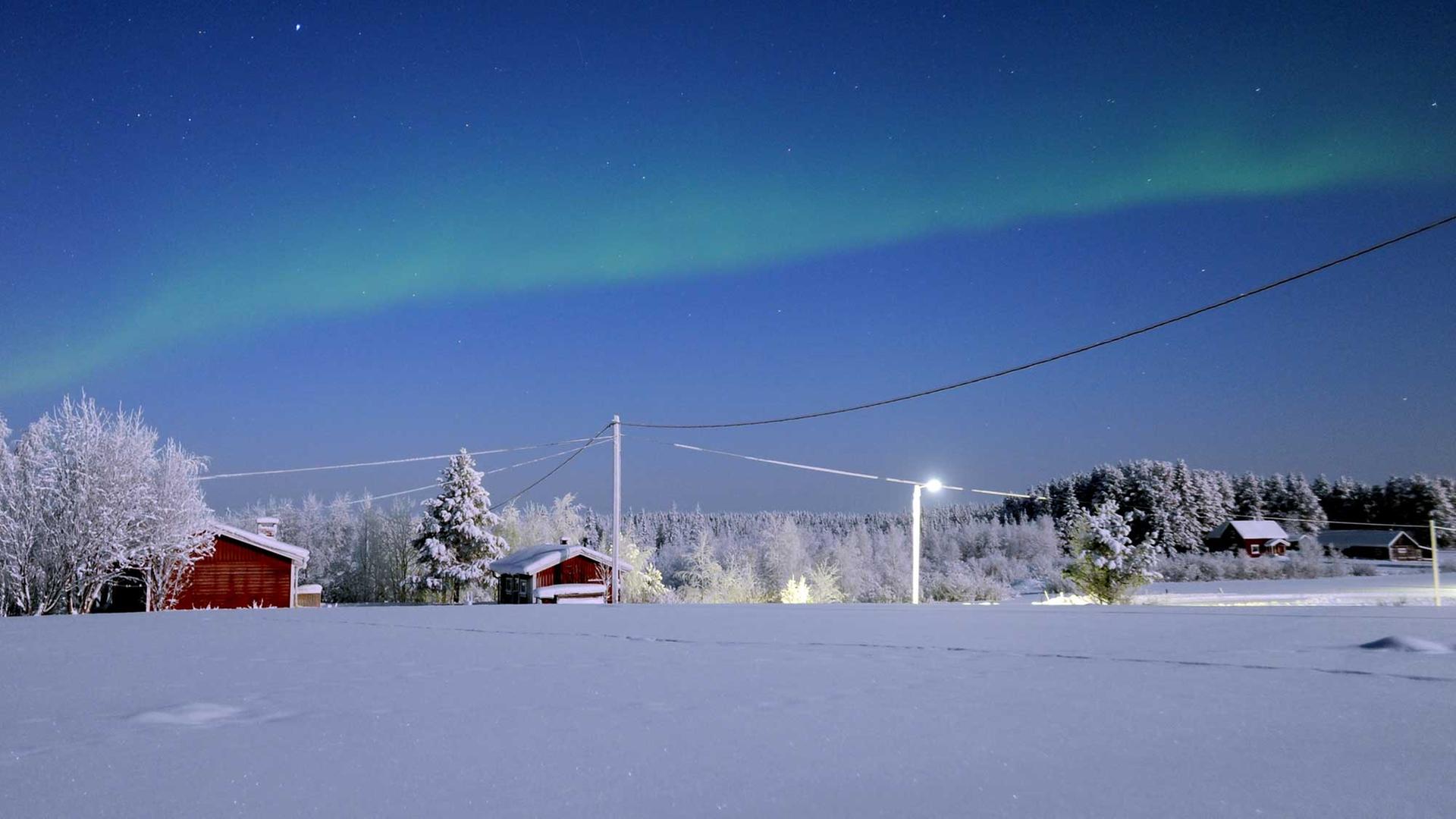 Eine verschneite Landschaft in Schweden, im Hintergrund einige Häuser.