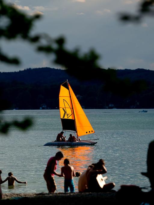 Ein kleines Segelboot fährt am 06.07.2014 in der Abendsonne in der Nähe von Kempfenhausen (Bayern) über den Starnberger See.