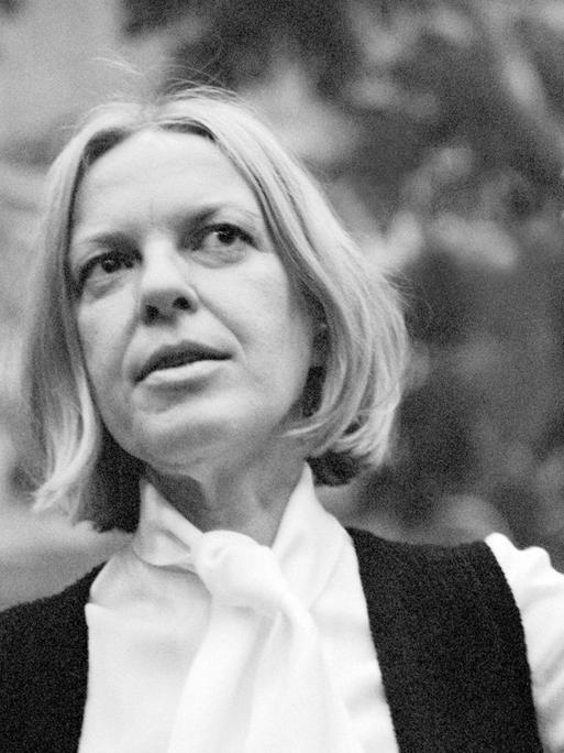 Ein Schwarzweiß-Foto zeigt die österreichische Lyrikerin Ingeborg Bachmann 1972 nach der Verleihung des Wildganspreises in weißem Hemd und schwarzer Weste auf einer Bank sitzend, die linke Hand erhoben gestikulierend, den Blick leicht lächelnd nach oben gerichtet.