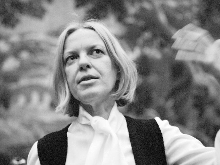 Ein Schwarzweiß-Foto zeigt die österreichische Lyrikerin Ingeborg Bachmann 1972 nach der Verleihung des Wildganspreises in weißem Hemd und schwarzer Weste auf einer Bank sitzend, die linke Hand erhoben gestikulierend, den Blick leicht lächelnd nach oben gerichtet.