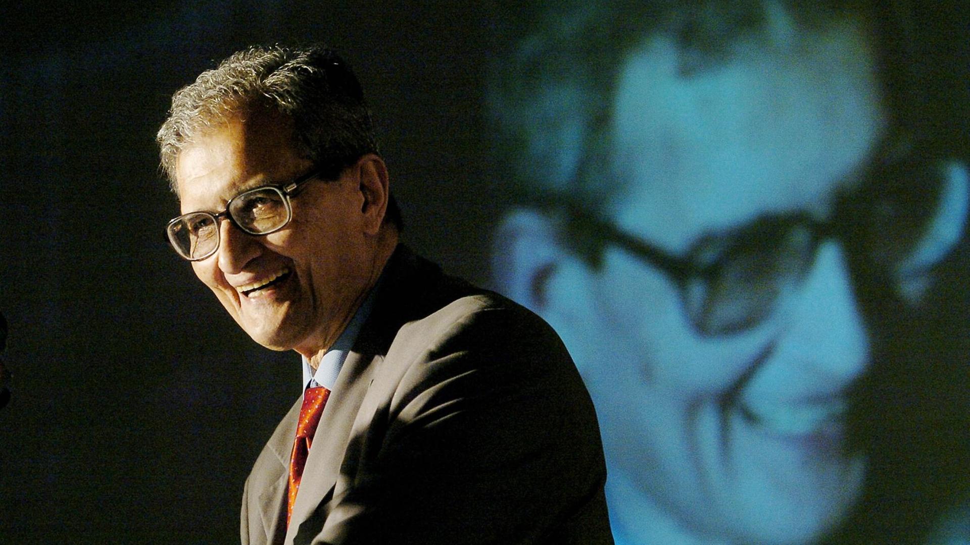 Amartya Sen hält eine Rede, im Hintergund wird sein Gesicht eingeblendet.