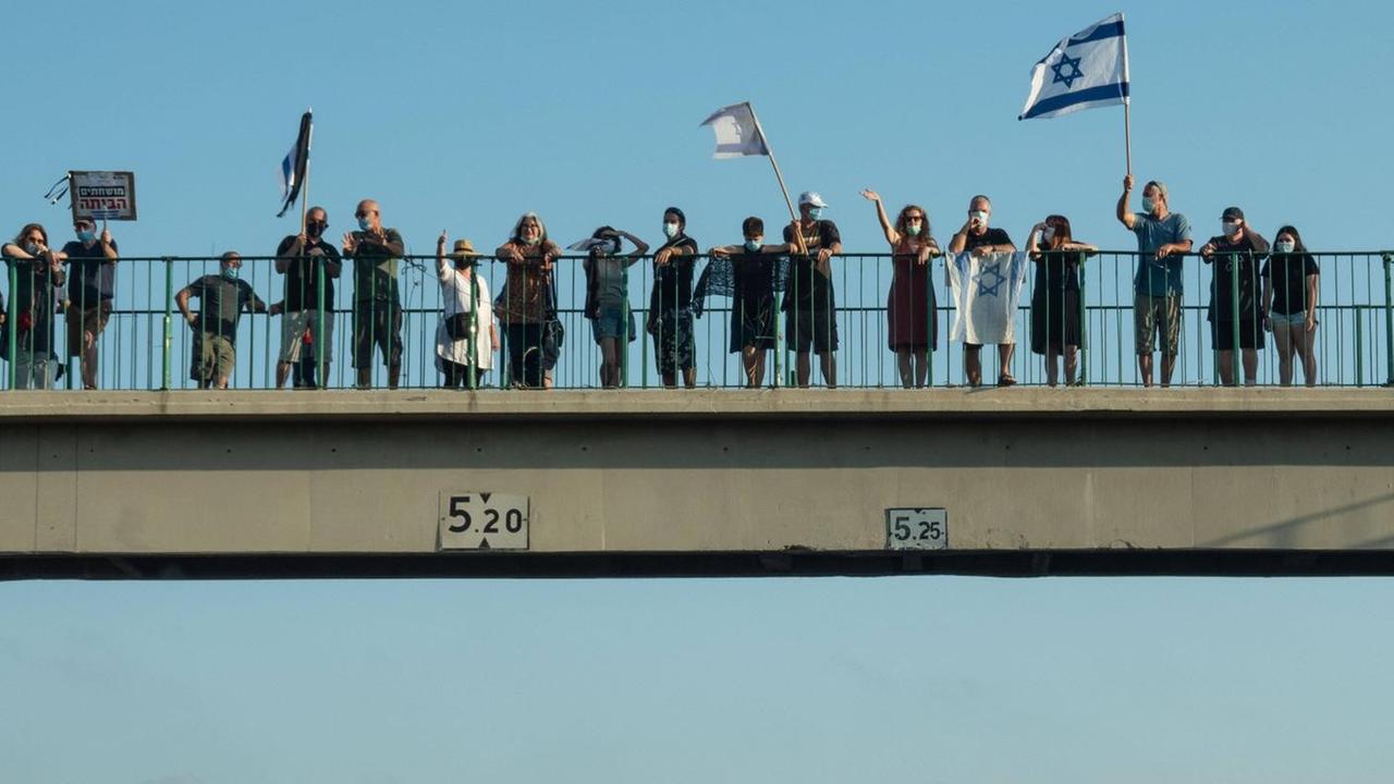 Auf einer Autobahnbrücke stehen Menschen und schwenken die israelische Flagge.