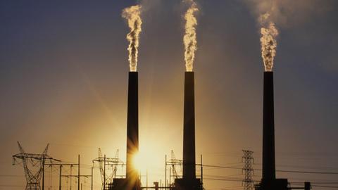 Emissionen aus einem Kohlekraftwerk. Der Rauch zieht aus drei Schornsteinen in den dunklen Himmel.