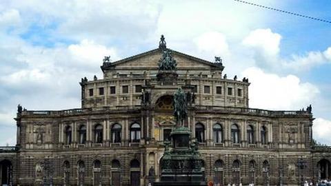 Touristen laufen in Dresden vor der Semperoper über den Theaterplatz mit dem König-Johann-Denkmal