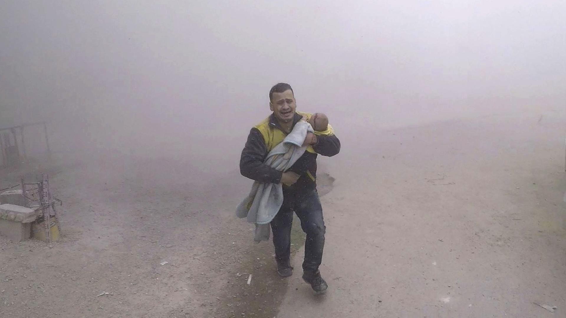 Das vom Syrischen Zivilschutz bereitgestellte Foto zeigt einen Notarzt, der seinen verletzten Sohn nach einem Luftangriff auf einen von Rebellen kontrollierten Vorort von Damaskus wegbringt.