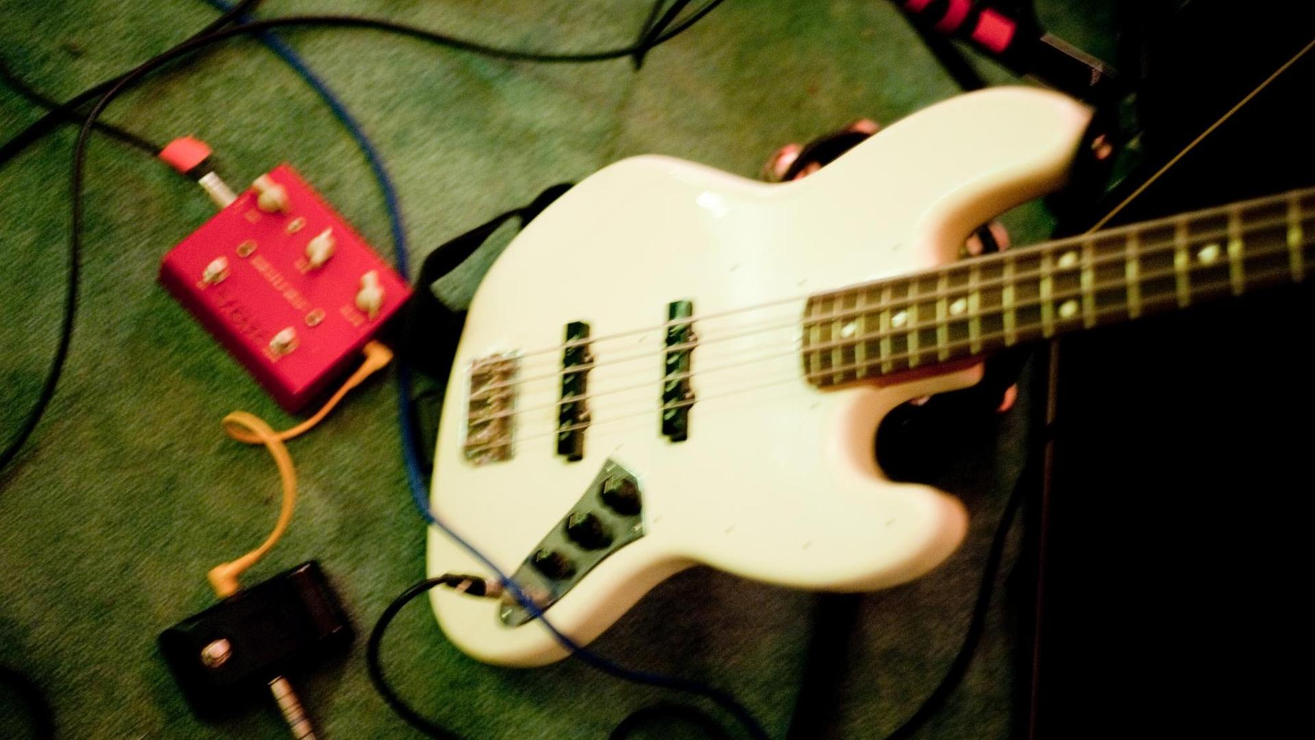 Ein weißer E-Bass (Model Fender Jazz Bass) steht neben einem Effektgerät auf einem Teppich in einem Proberaum in Berlin-Lichtenberg.