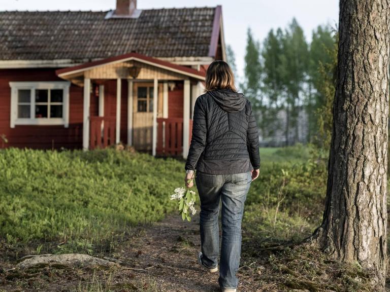 Eine Frau geht auf eine rote Holzhütte im Wald bei Kuopio in Finnland zu
