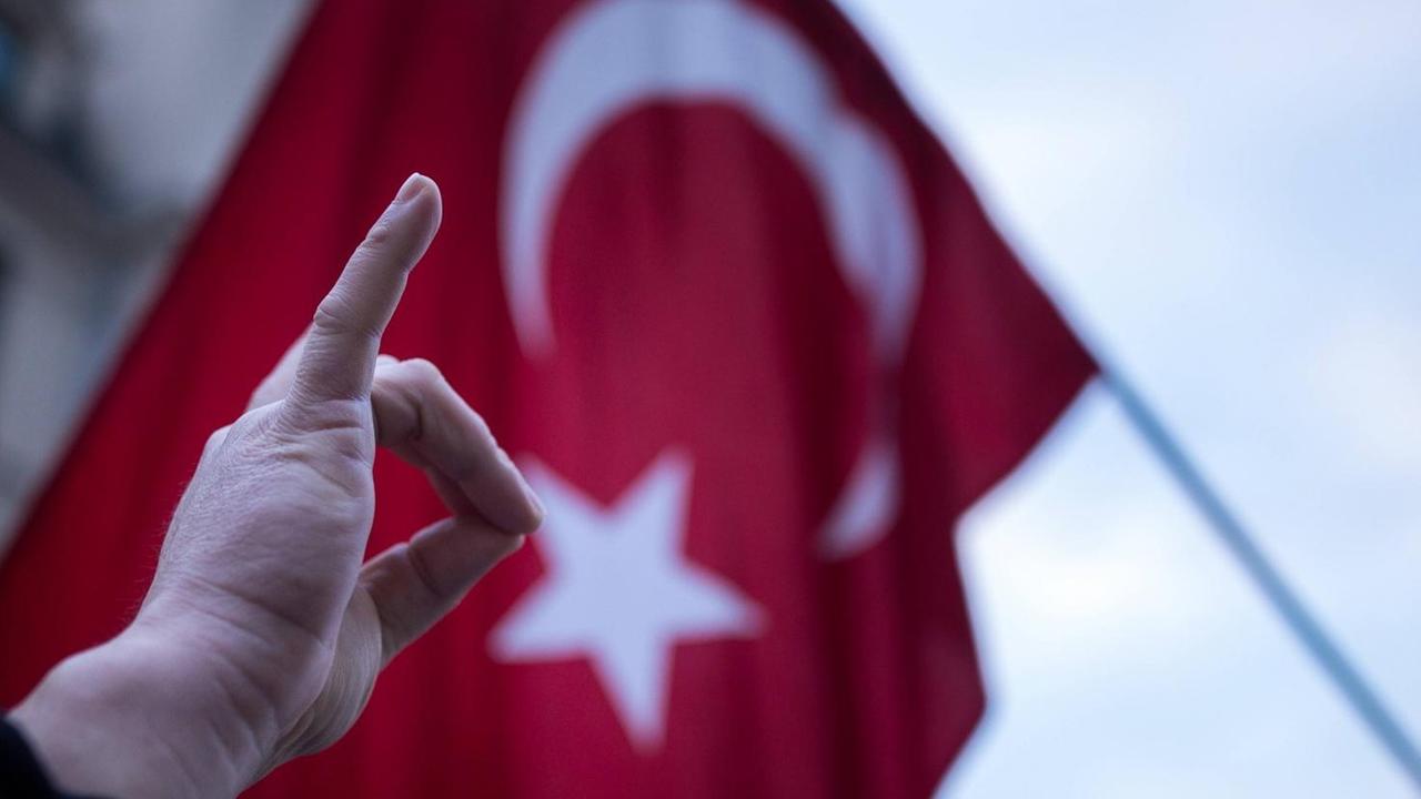 Eine Hand formt den sogenannten Wolfsgruss vor einer türkischen Flagge.