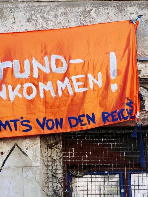 Ein Transparent mit der Aufschrift "Grundeinkommen! Nehmt's von den Reichen" hänft in Berlin an einem unsanierten und besetzten Haus in der Linienstrasse im Bezirk Mitte.
