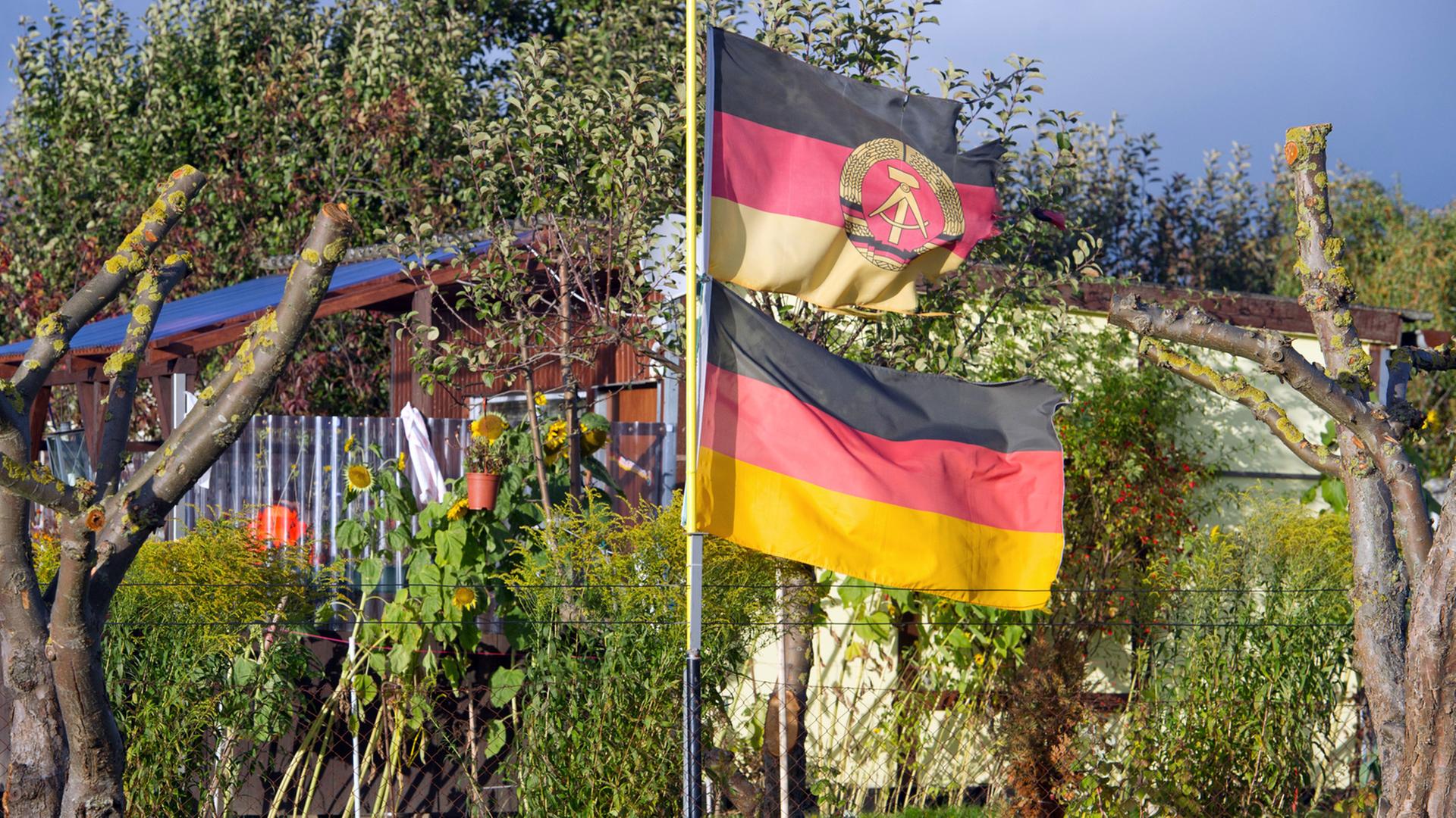 Eine DDR-Fahne und eine Deutschland-Flagge wehen an einem Fahnenmast in der Kleingartenanlage "Samtenser Frühling" in Samtens auf der Ostseeinsel Rügen.