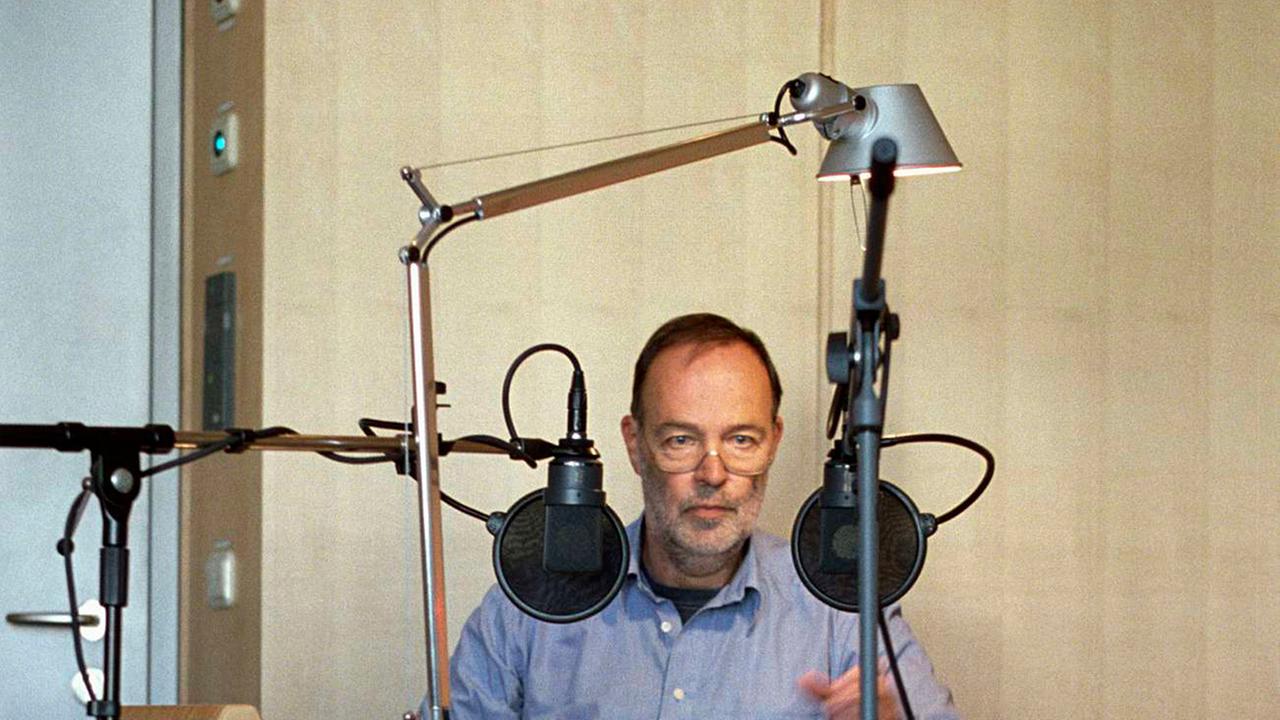 Der Autor Karl-Heinz Stevens sitzt im Studio an einem Tisch mit Mikrofon.