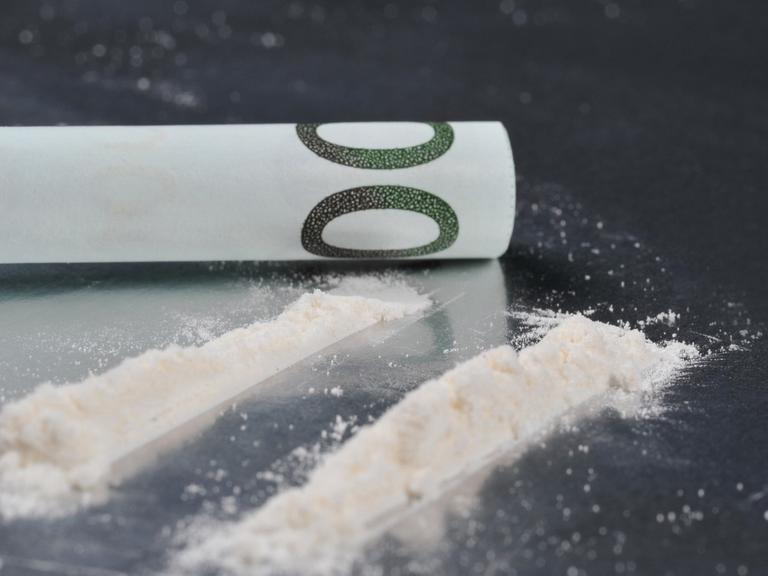 Ein zusammengerollter Geldschein neben zwei Linien Kokain