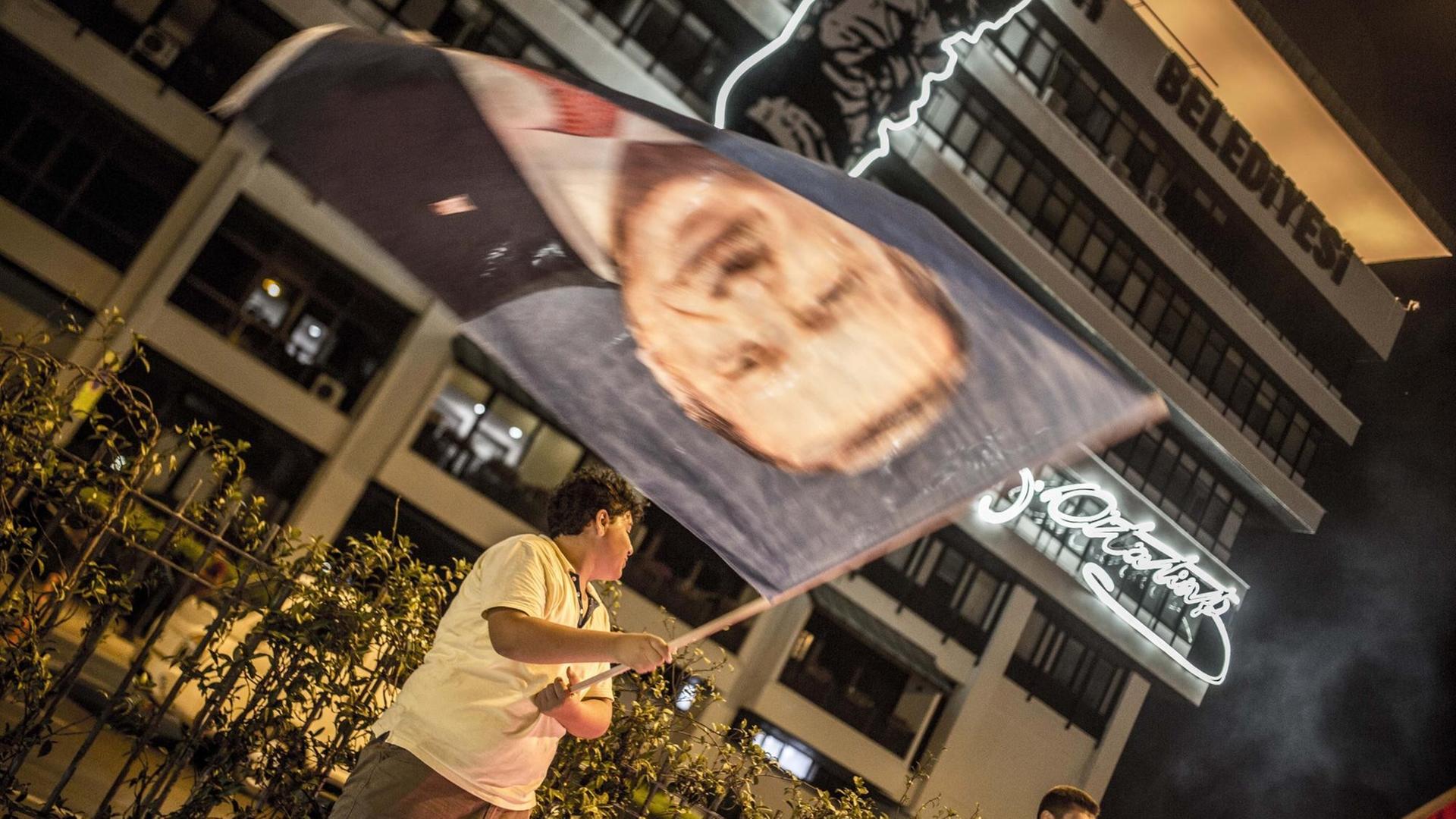 Ein junger Mann schwenkt eine riesige Fahne mit dem Konterfei des gewählten Präsidenten.