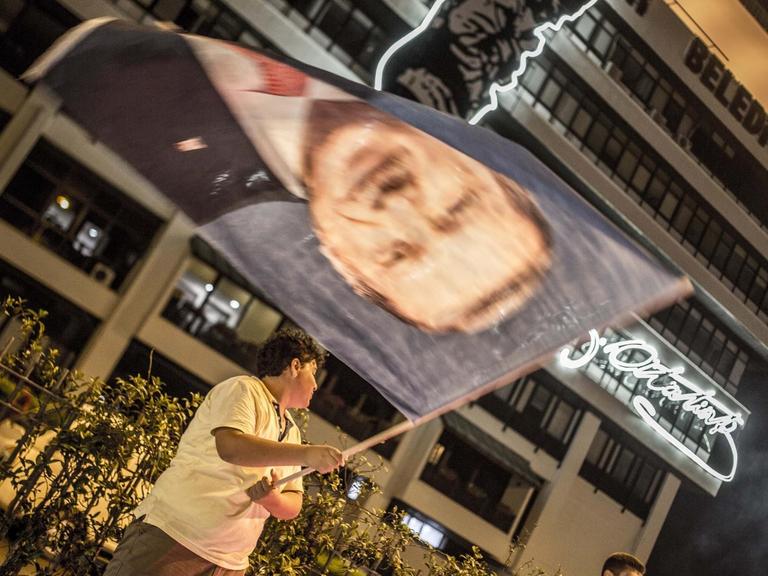 Ein junger Mann schwenkt eine riesige Fahne mit dem Konterfei des gewählten Präsidenten.