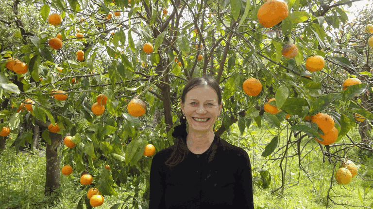 Die Tänzerin Sighilt Pahl steht vor einem Orangenbaum und lächelt in die Kamera.