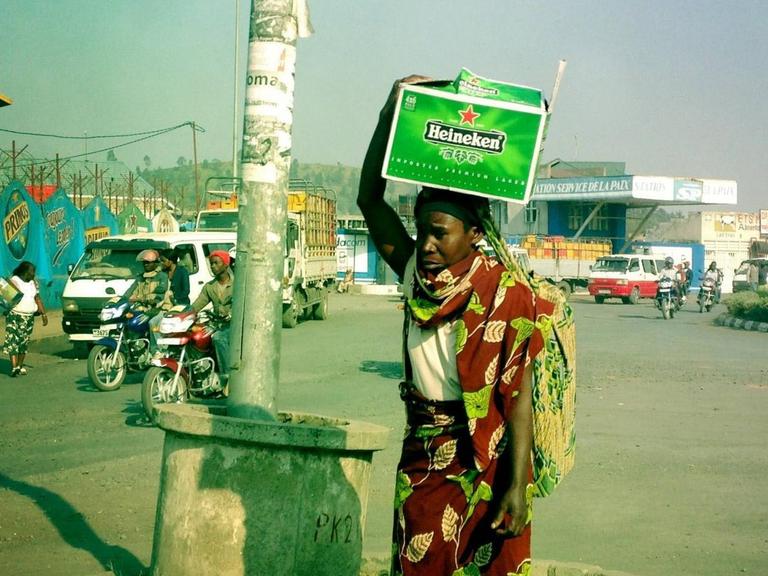 Eine Frau steht auf einer Verkehrsinsel in Goma im Kongo und trägt eine Kiste mit Heineken-Bier auf dem Kopf, aufgenommen 2013