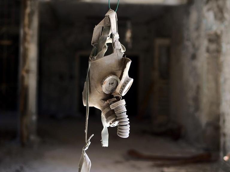 Eine Gasmaske hängt in einem Gang eines zerstörten Gebäudes von der Decke.