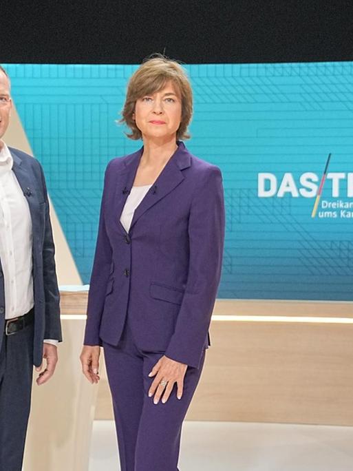 Die Moderatoren Oliver Köhr und Maybrit Illner stehen im Fernsehstudio.