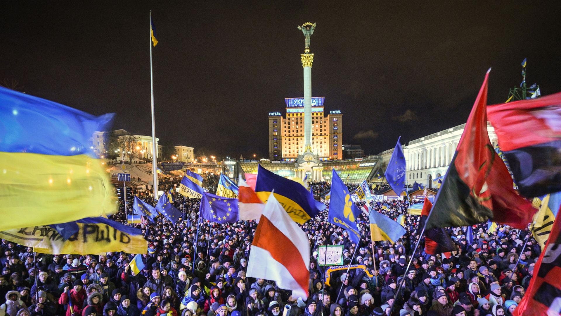 Auf dem zentralen Platz Maidan in der ukrainischen Hauptstadt Kiew demonstrieren bei Nacht hunderte Menschen und schwenken Flaggen.