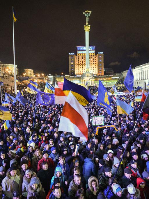 Auf dem zentralen Platz Maidan in der ukrainischen Hauptstadt Kiew demonstrieren bei Nacht hunderte Menschen und schwenken Flaggen.