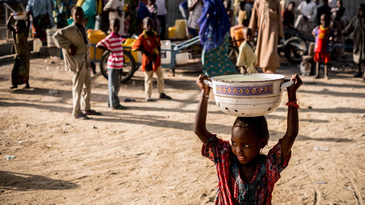 Ein nigerianisches Mädchen trägt eine Schale mit Wasser im Muna Dalti UNICEF-Lager bei Maiduguri