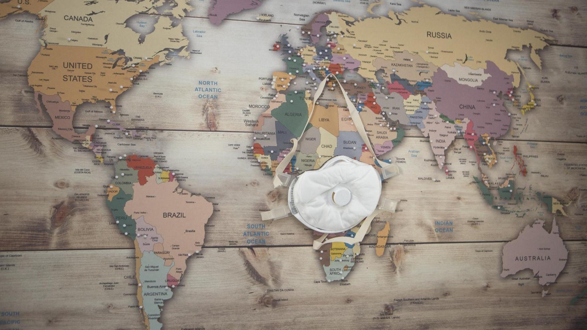 An einer Wand mit Weltkarte ist eine Atemschutzmaske angepinnt.