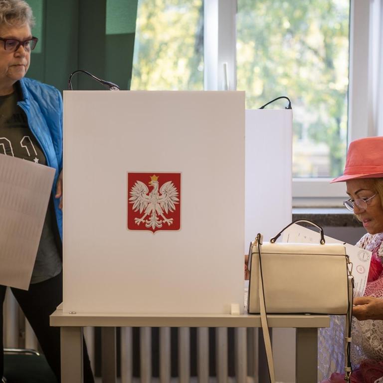 Zwei Frauen, eine stehend, eine sitzend, mit Wahlzettel in einem Wahlbüro in Warschau. 