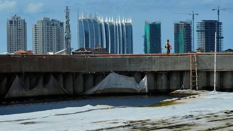 Ein Arbeiter geht an einer Wand entlang, die als Barriere verwendet wird, um zu verhindern, dass Meerwasser an Land fließt