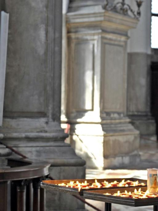Frau im Gebet mit Kerzen vor Jesus am Kreuz, im Kirchenschiff der Santa Maria della Salute in Venedig, Italien.