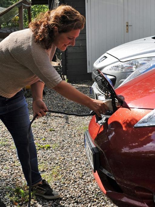 Eine Frau steckt ein Kabel in ihren Elektro-Nissan, um das Auto zu laden.