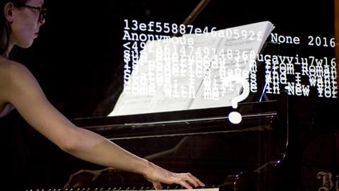 Eine Pianistin spielt am Flügel, während Zifferncodes und Wörter auf die Szene proojiziert werden
