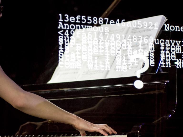 Eine Pianistin spielt am Flügel, während Zifferncodes und Wörter auf die Szene proojiziert werden