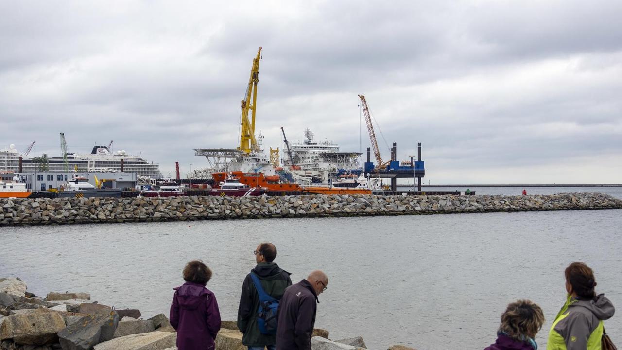 Menschen blicken auf den Fährhafen Mukran, auf dem zwei russische Schiffe für den Weiterbau der Nordstream 2 Pipeline vorbereitet werden.