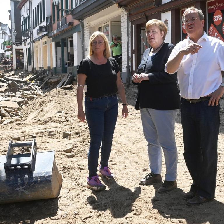 Bundeskanzlerin Angela Merkel steht mit NRW-Ministerpräsident Armin Laschet und der Bürgermeisterin von Bad-Münstereifel in einer zerstörten Straße