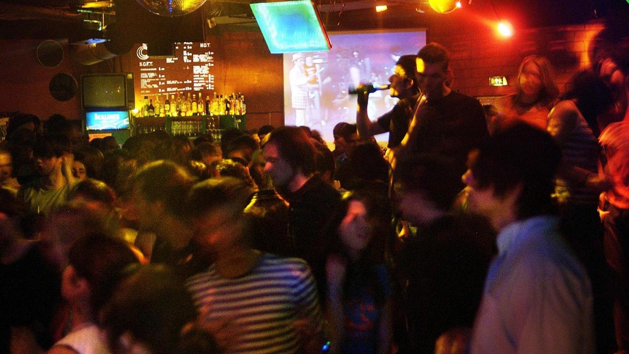 Viele Menschen dicht gedrängt auf einer Tanzfläche, im Hintergrund Bildschirme und eine Bar.
