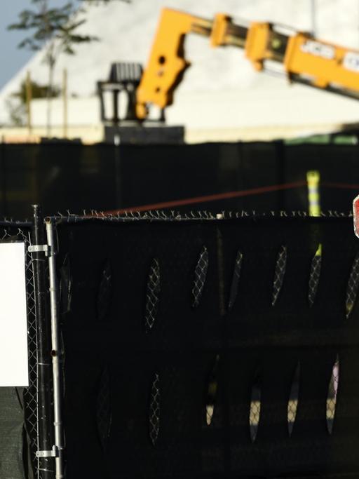 Ein Arbeiter steht an einem Tor zur Baustelle mit "Stop"-Schild, damit niemand ohne Temperaturmessung auf das Gelände kommt.