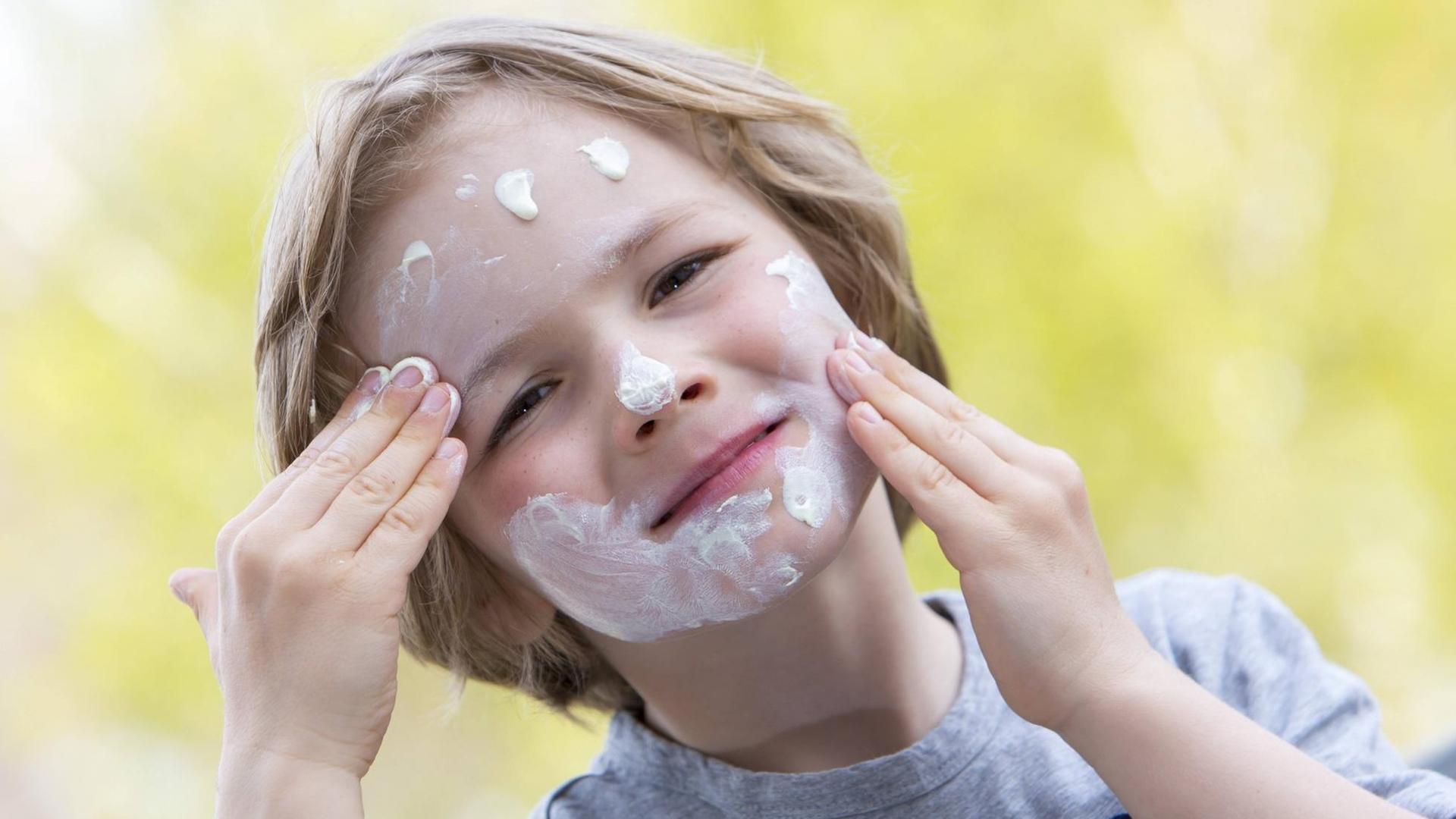 Kleiner Junge trägt sich selber Sonnencreme, im Gesicht auf.