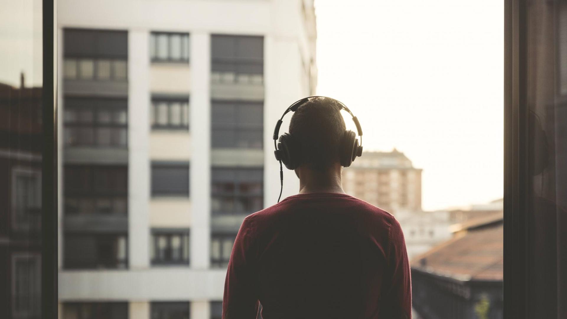 Ein Mann mit Kopfhörer steht am Fenster.