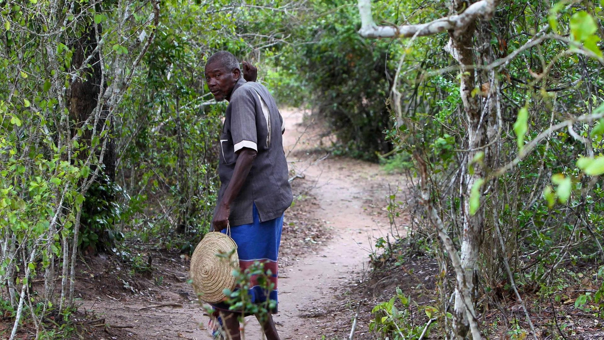 Ein Mann trägt eine runde Basttasche in der Hand und geht auf einem schmalen Pfad in den Kaya-Wald